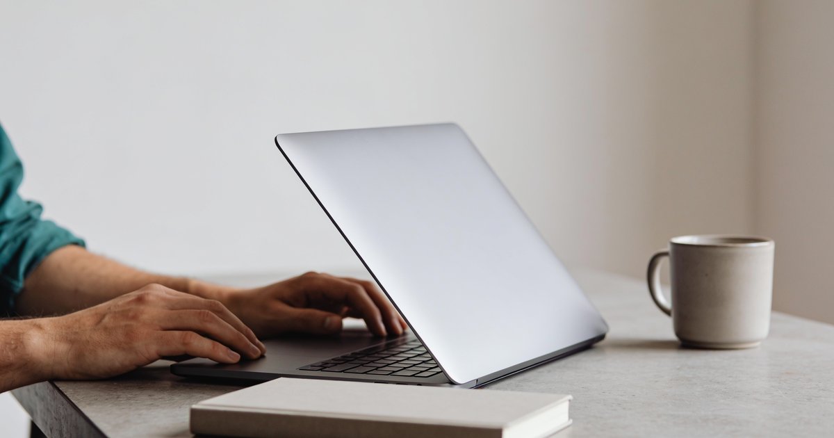 Hände am Schreibtisch bei der WordPress-Wartung, Notizbuch und Laptop