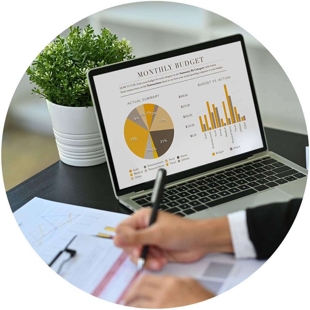 Eine Person überprüft Papiere mit Diagrammen, während sie vor einem Laptop sitzt, auf dem ein Bericht zum „Monatsbudget“ angezeigt wird, der für Telefonmarketing-Strategien von entscheidender Bedeutung ist. Der Bildschirm zeigt ein Kreisdiagramm und ein Balkendiagramm mit Finanzdaten. Im Hintergrund auf dem Schreibtisch steht friedlich eine Topfpflanze.