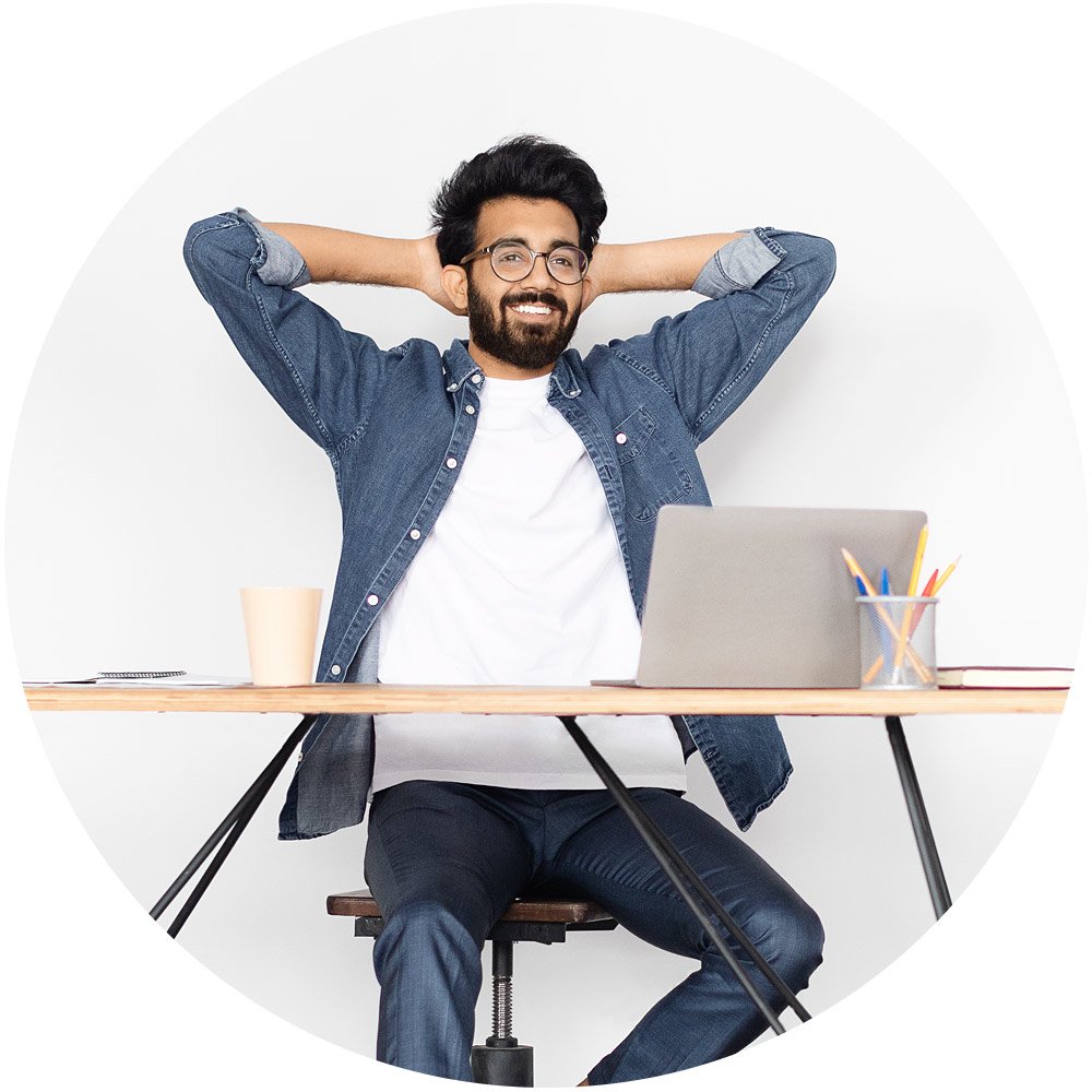 Ein Mann sitzt mit einem Laptop und einer Tasse an einem Schreibtisch und lächelt unbeschwert, während er den neuesten Chatbot-Dienst nutzt. Er trägt ein Jeanshemd und eine Brille und hat die Hände entspannt hinter dem Kopf. Bunte Bleistifte in einem Halter verleihen dem schlichten weißen Hintergrund Lebendigkeit.