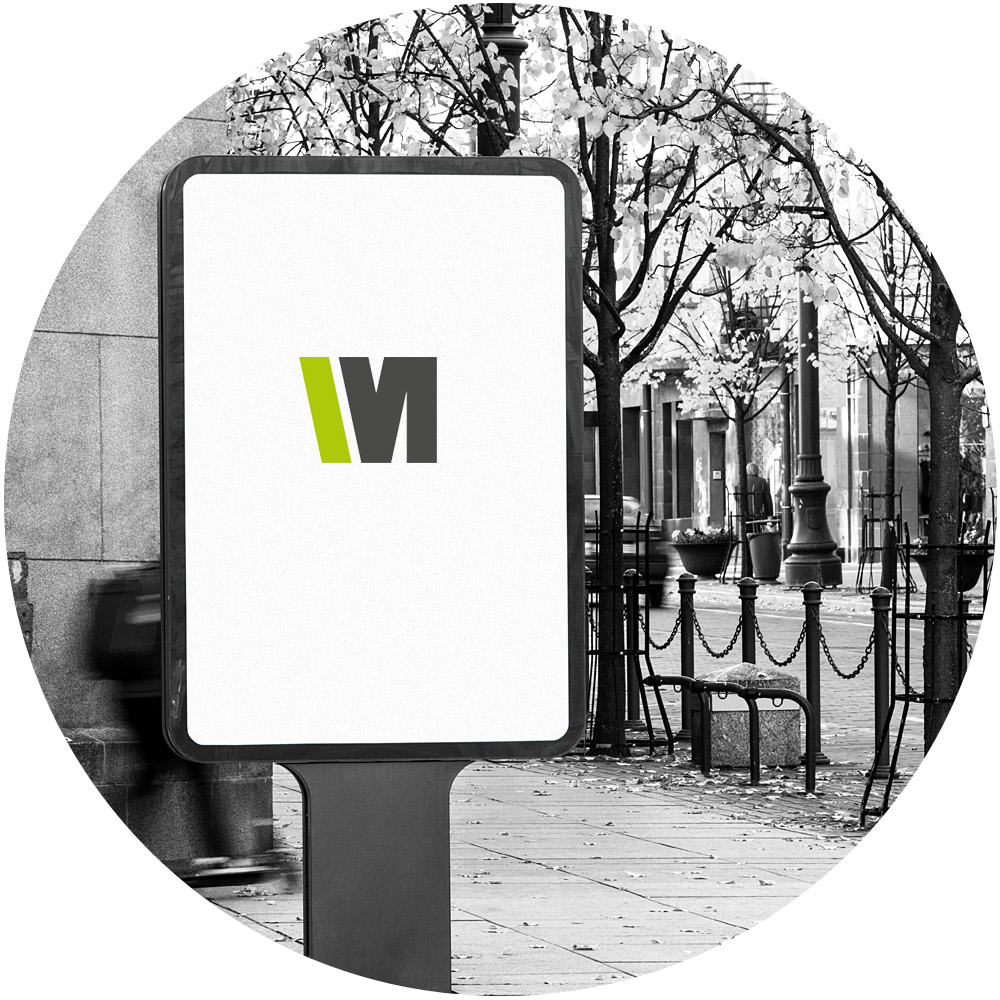 Ein kreisförmiges Schwarzweißbild zeigt eine Außenwerbeanzeige mit einem Logo. Die digitale Anzeige zeigt ein grün-schwarzes stilisiertes „W“ und „M“ auf einem leeren weißen Hintergrund. Die Umgebung bietet eine hervorragende Serviceästhetik und umfasst Bäume, einen Bürgersteig und Laternenpfähle.