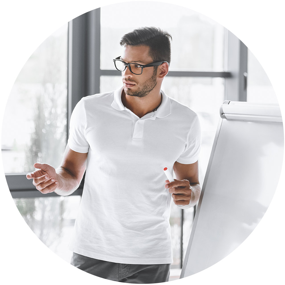 Ein Mann in weißem Poloshirt und Brille steht mit einem Marker in der Hand vor einem Flipchart. Er scheint in einem hellen Raum mit großen Fenstern Marketing-Funnels zu erklären.