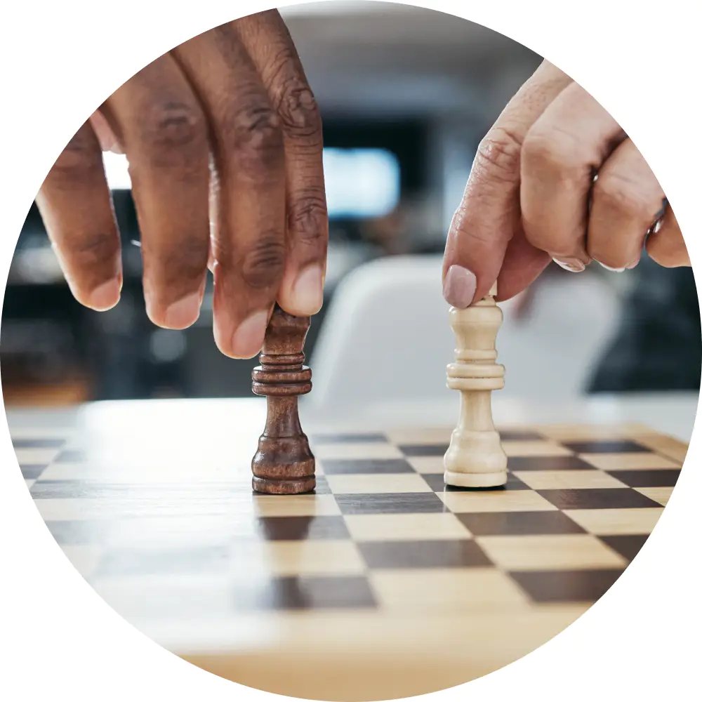 Zwei Hände über einem Schachbrett, jede hält eine Königsfigur, eine schwarze und eine weiße, bereit zum Spiel. Der Hintergrund ist leicht verschwommen, sodass die Aufmerksamkeit des Betrachters auf die Schachfiguren und den strategischen Moment der Überwachung des nächsten Zugs gelenkt wird.