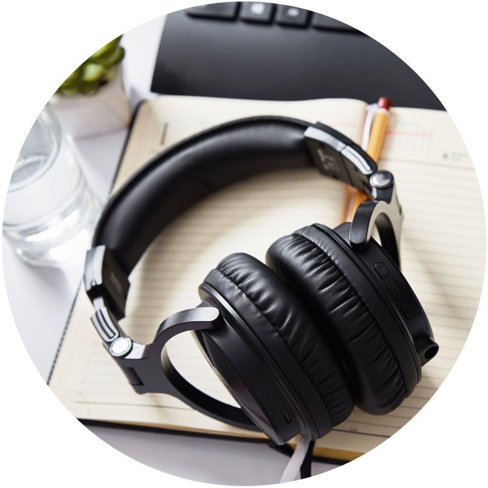 Schwarze Over-Ear-Kopfhörer liegen auf einem offenen Notizbuch mit einem Bleistift, perfekt für das Brainstorming Ihres nächsten Podcasts. Im Hintergrund sind ein Glas Wasser und ein Teil einer Tastatur zu sehen, was ein ideales Service-Layout für Kreativität ergibt.