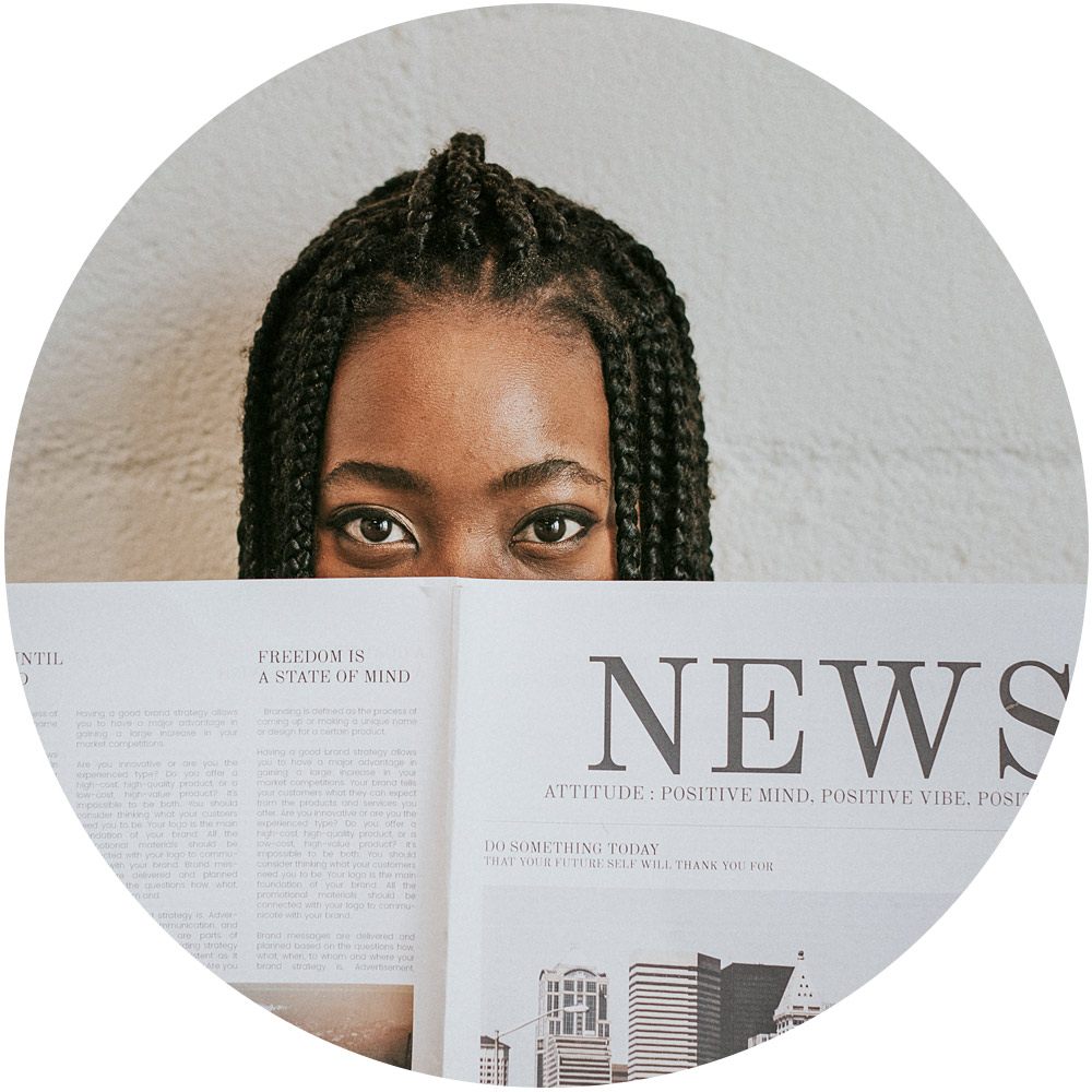 Eine Person mit geflochtenem Haar blickt über eine Zeitung und zeigt zwischen Schlagzeilen und Text nur ihre Augen. Diese Szene spiegelt die Nuancen der Pressearbeit vor dem Hintergrund einer strukturierten, hellen Wand wider.