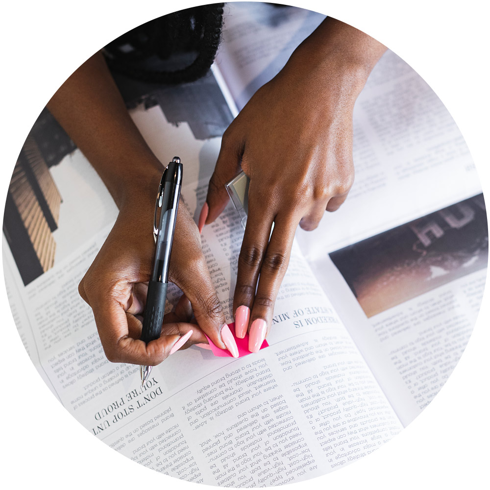 Eine Person mit rosa Nägeln hält einen Stift und zeigt auf einen Abschnitt in der Zeitung, was darauf schließen lässt, dass sie das gedruckte Material aufmerksam liest oder Anmerkungen macht. Diese Szene ruft Themen wie Presse und Öffentlichkeitsarbeit hervor und unterstreicht die Auseinandersetzung mit dem öffentlichen Diskurs.