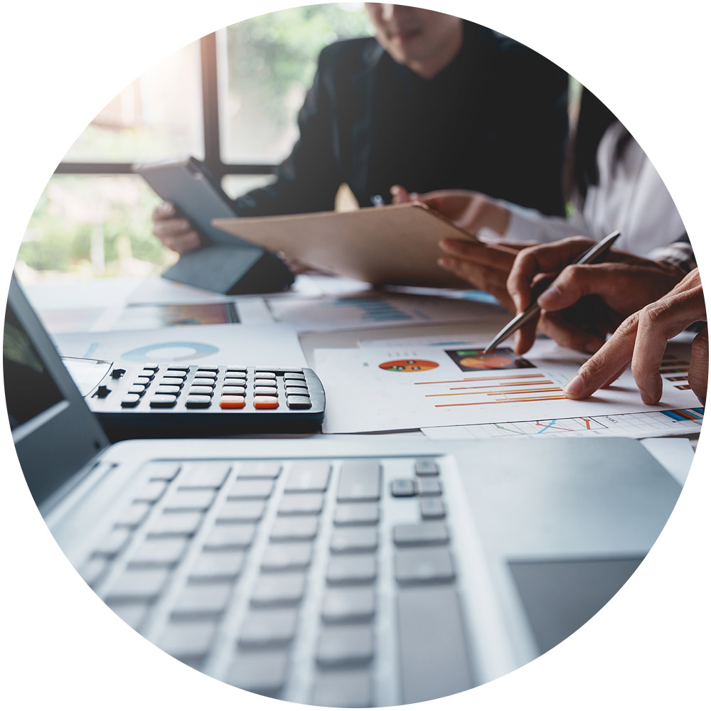 Eine Gruppe von Personen sitzt mit Laptops, Dokumenten und einem Taschenrechner an einem Tisch und diskutiert intensiv. Dabei zeigen sie auf Diagramme und Grafiken auf den Papieren. Ihr Fokus liegt darauf, während dieses kollaborativen Geschäftstreffens, das durch präzise Datenanalysen unterstützt wird, wichtige Erkenntnisse zu berichten.