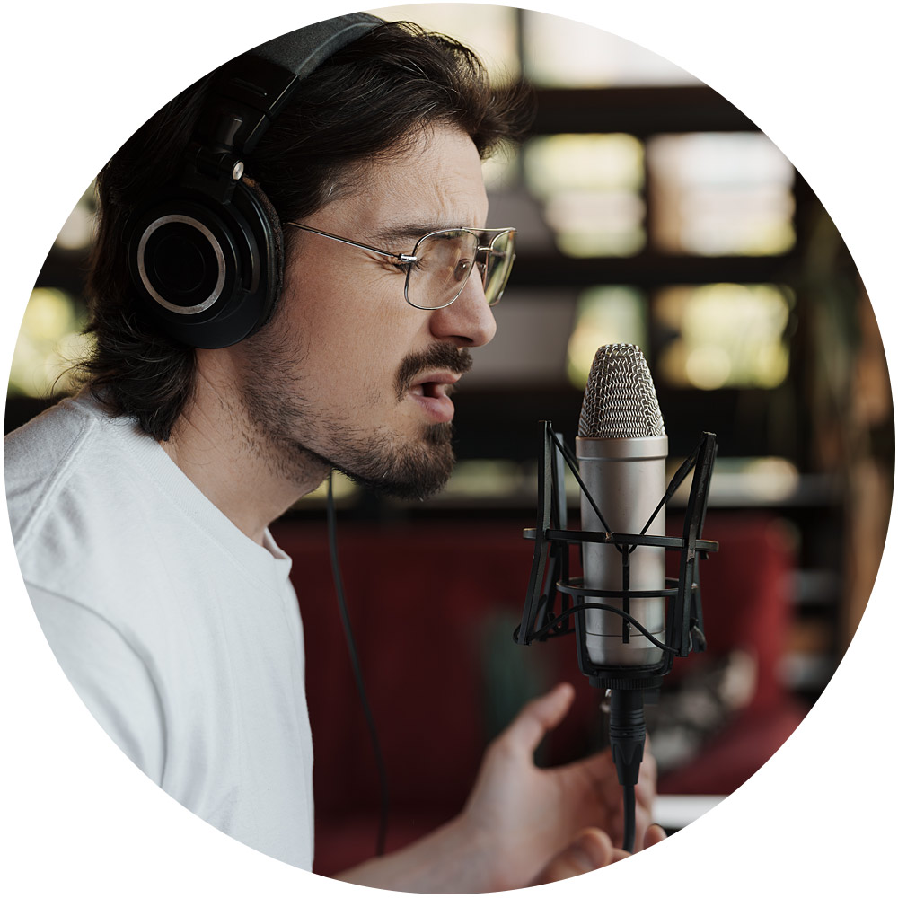 Eine Person mit Kopfhörern und weißem Hemd singt in einem Aufnahmestudio leidenschaftlich in ein Mikrofon. Der leicht verschwommene Hintergrund unterstreicht den Fokus auf die Person, während sie die Tiefen der Stimmklontechnologie erforscht, um einzigartige Stimmnuancen zu reproduzieren.