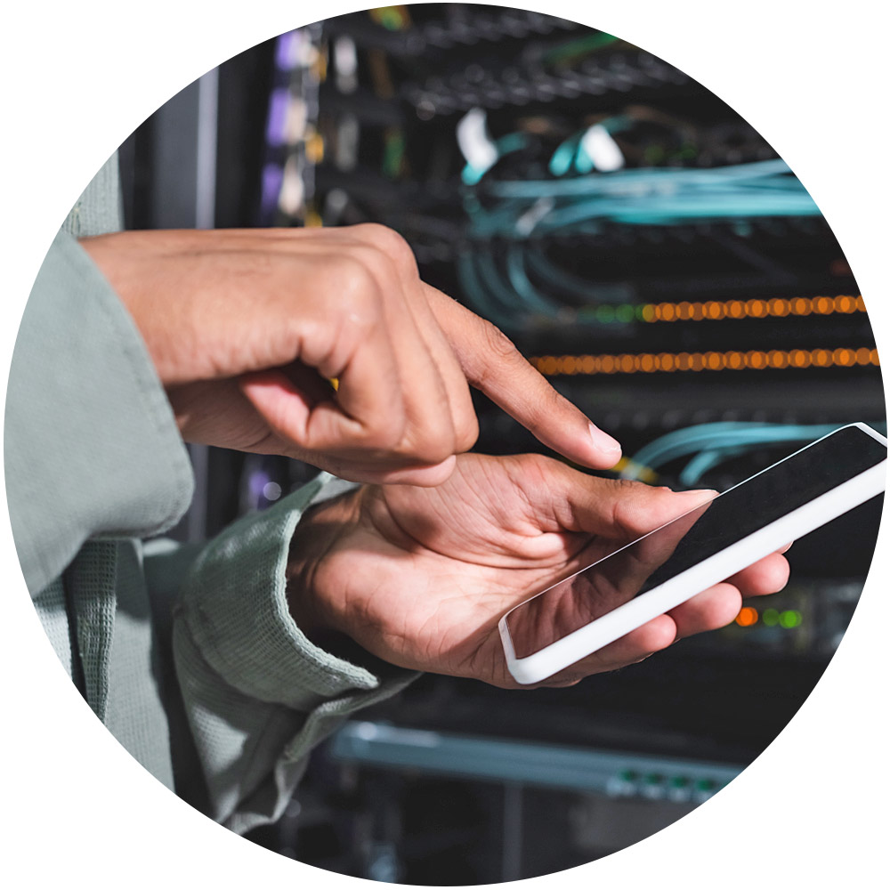 Eine Person hält ein Smartphone in beiden Händen vor einem Server-Rack und ist damit beschäftigt, die Leistung einer Website zu analysieren. Die Person, in ein langärmliges Kleidungsstück gekleidet, navigiert durch SEO-Tools, während im unscharfen Hintergrund die Netzwerkausrüstung leise brummt.