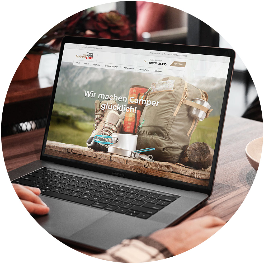 Eine Person sitzt mit einem Laptop an einem Schreibtisch und durchsucht eine Website, die einen Service anbietet, der verspricht: „Wir machen Camper glücklich!“ Auf dem Bildschirm werden Campingausrüstungen wie Rucksäcke, Stiefel und Kochgeschirr präsentiert.